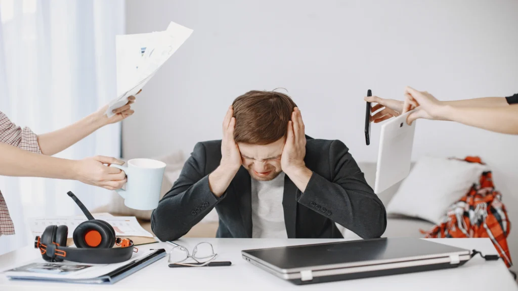 Overwhelmed employee covering his ears while facing multiple workplace demands