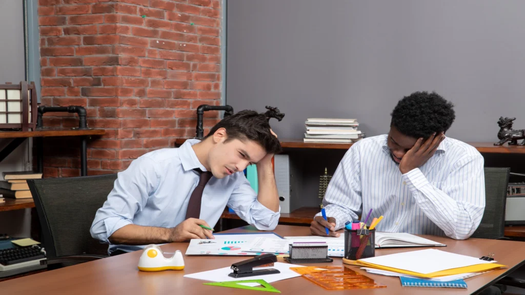 Two employees appearing mentally exhausted while working at a desk