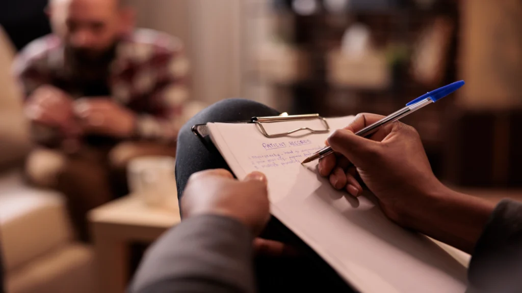 Therapist taking notes while listening to a client during a counseling session